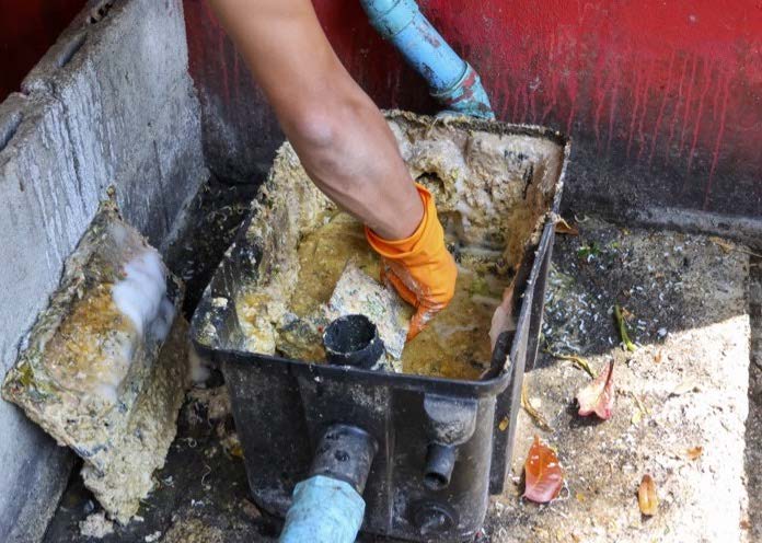 Person cleaning a clogged grease trap with a gloved hand.